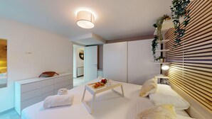 A modern bedroom with a bed, bedside tables, a small table with items, and a wall-mounted shelf with plants. - Harmonia Cottage by Bookinggardalake (Soiano del Lago)