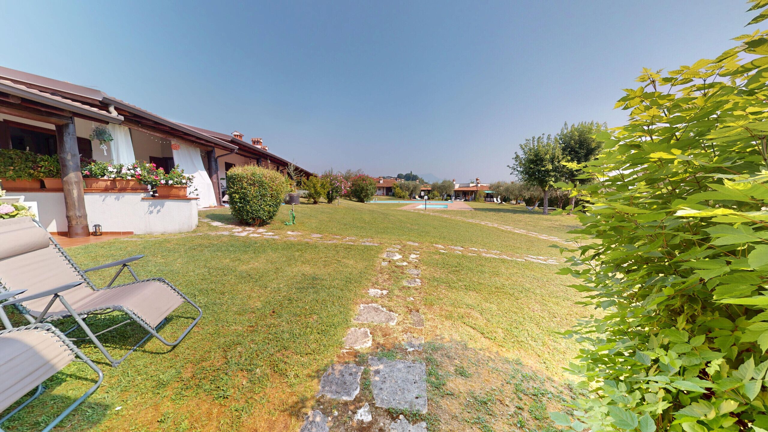 A residential property with a lawn, a swimming pool, and a patio area with outdoor furniture.