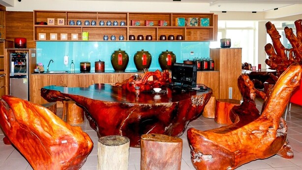 Un comedor con una mesa y sillas de madera únicas, una cocina al fondo y estantes con objetos decorativos.