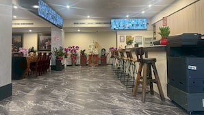 Un hall de hotel con mostrador de recepción, taburetes de bar, una impresora grande y una pantalla digital.
