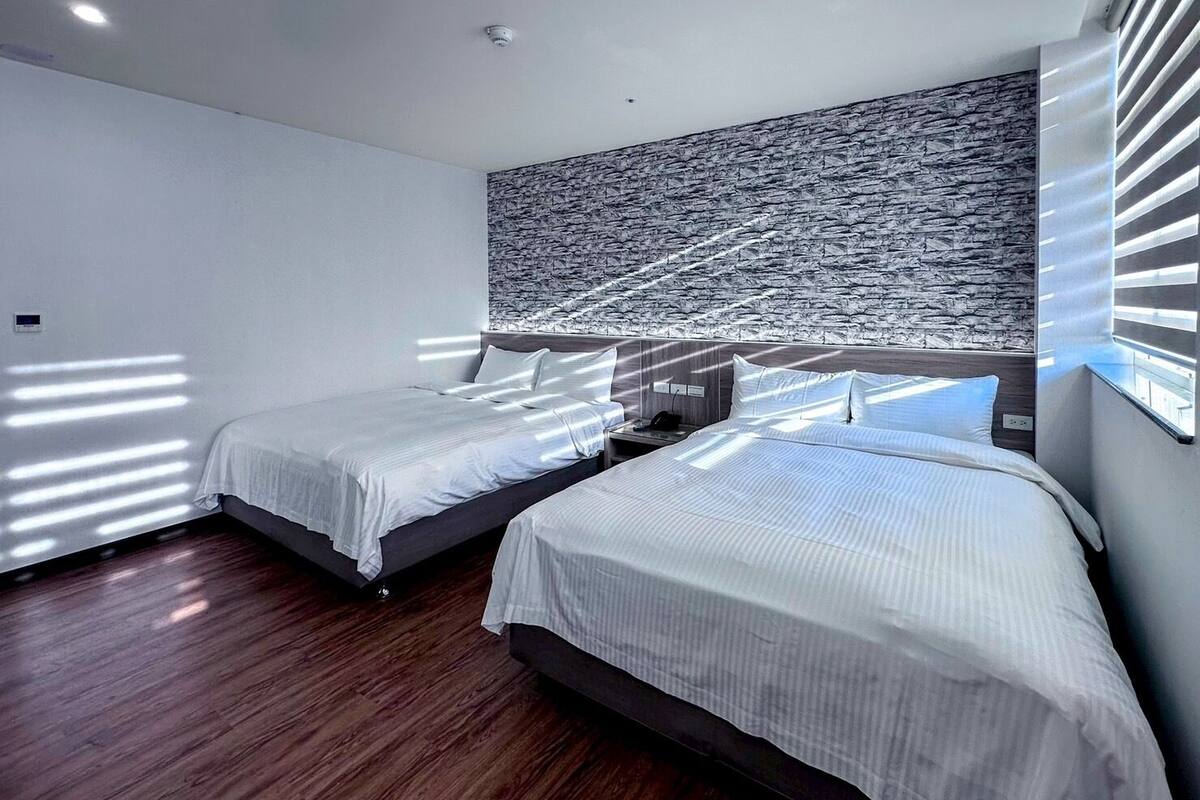 A modern hotel room with two beds, wooden flooring, and a large textured wall.