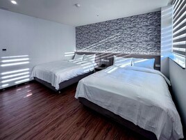 A modern hotel room with two beds, wooden flooring, and a large textured wall.