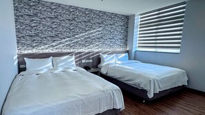 Habitación de hotel con dos camas, cabecera con textura de piedra, mesita de noche y ventana con persianas.
