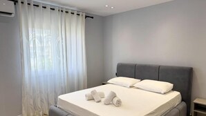 A modern bedroom with a large bed, grey upholstered headboard, and white linens.