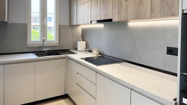 A modern kitchen with white cabinets, a black countertop, and a window with a view of greenery.