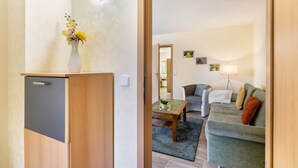 A room with a wooden cabinet, a vase with flowers, a table with a plant, a grey sofa, and a lamp. - Holiday Home Near Forest and Lake (Templin)