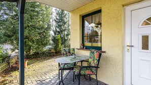 A covered patio with a table and chairs, a door, and a window overlooking a garden. - Holiday Home Near Forest and Lake (Templin)