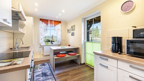A modern kitchen with a sink, stove, and microwave. There is a window with a view of greenery outside. - Holiday Home Near Forest and Lake (Templin)