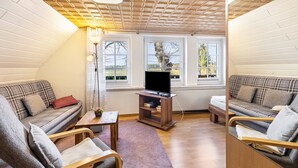 A cozy living room with a sofa, armchair, TV stand, and large windows. - Apartment 'Für Monteure' with Wi-Fi (Templin)