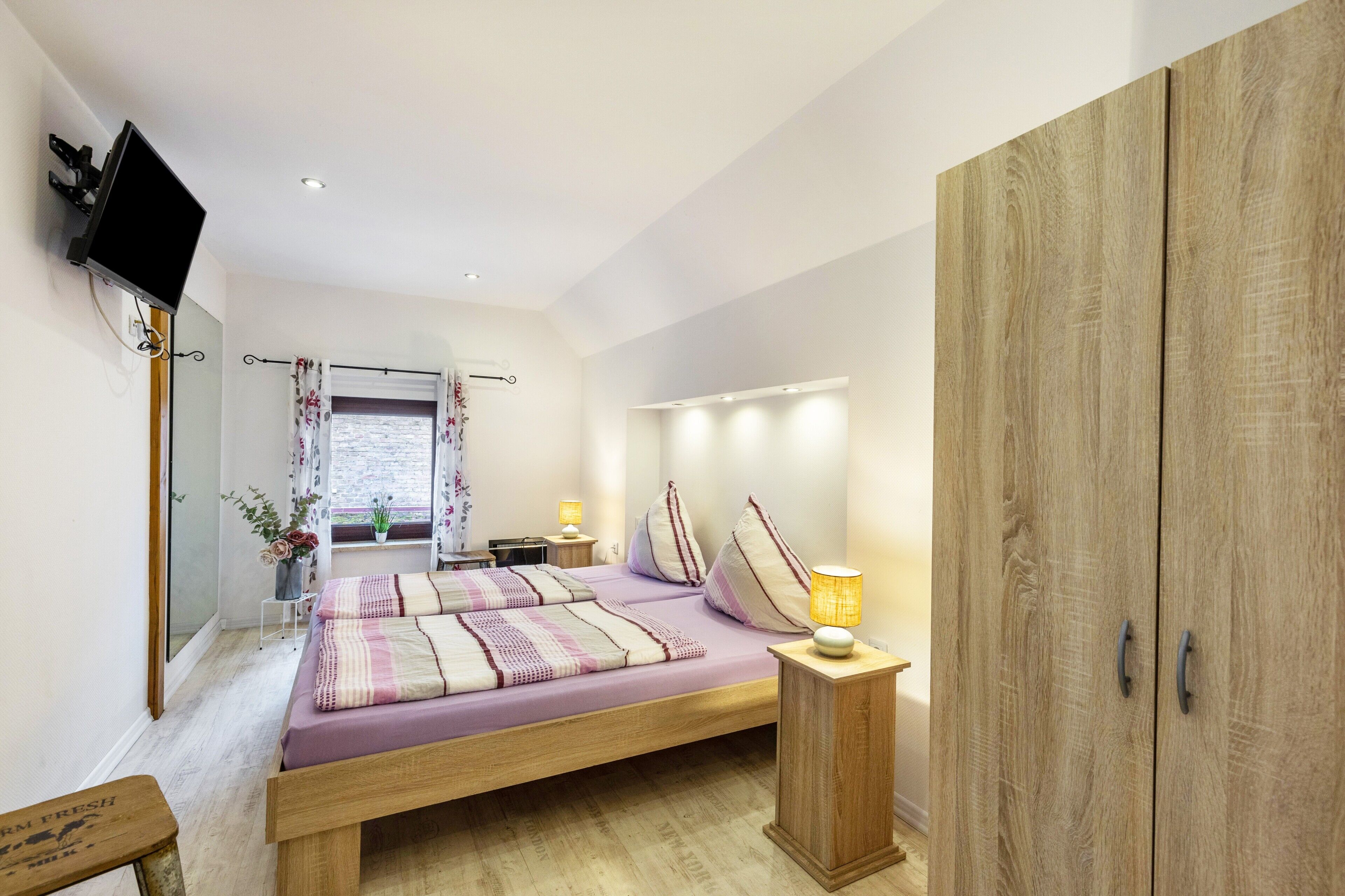 Une chambre à coucher comprenant un lit, un téléviseur fixé au mur, une armoire et une table de chevet avec une lampe.