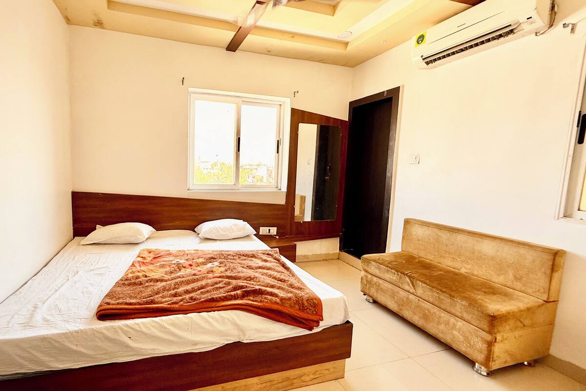 A bedroom with a bed, a window, a sofa, and an air conditioning unit.