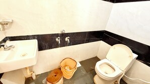 Une petite salle de bain avec un lavabo blanc, des toilettes et un seau posé sur le sol.