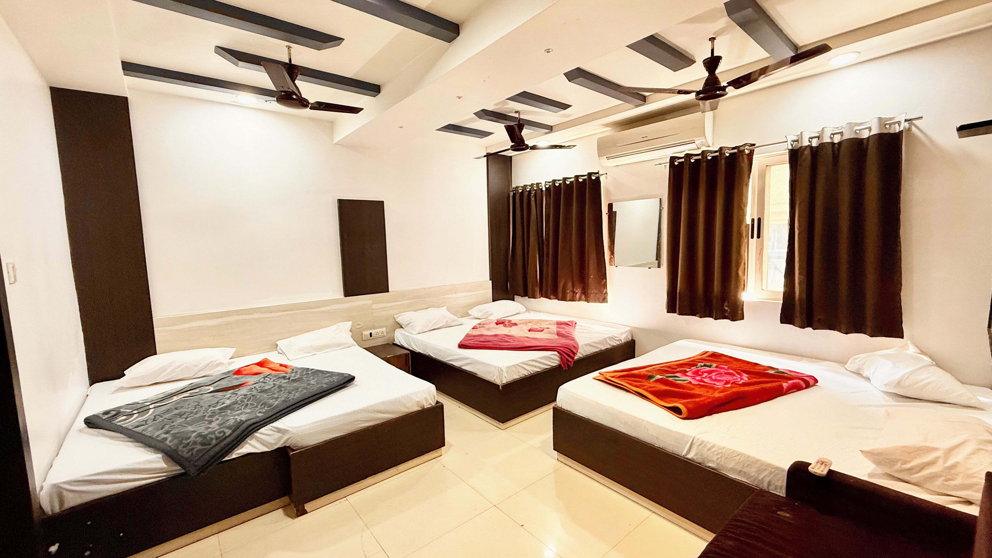 A hotel room with three single beds, a ceiling fan, a large mirror, and a window with curtains.