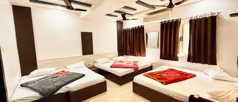 A hotel room with three single beds, a ceiling fan, a large mirror, and a window with curtains.