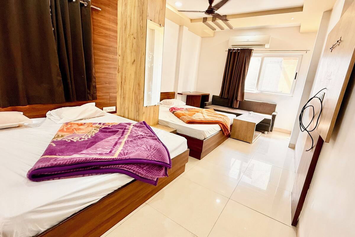 A modern hotel room with two beds, a sofa, a small table, and a ceiling fan.