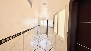 Un couloir carrelé, avec une porte sur la droite et une fenêtre au fond.
