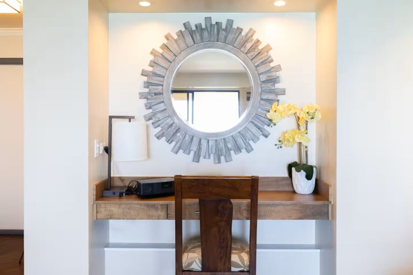 A modern vanity with a circular mirror, wooden countertop, and a chair.