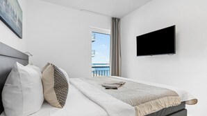 A hotel room with a bed, a TV, a painting, and a view of the sea. - Portus - Sea view, balcony, barbecue, walk-in shower, fireplace (Olpenitz)