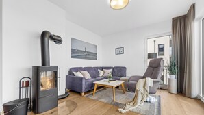 A modern living room with a fireplace, a sofa, a coffee table, and a large window with curtains. - Portus - Sea view, balcony, barbecue, walk-in shower, fireplace (Olpenitz)