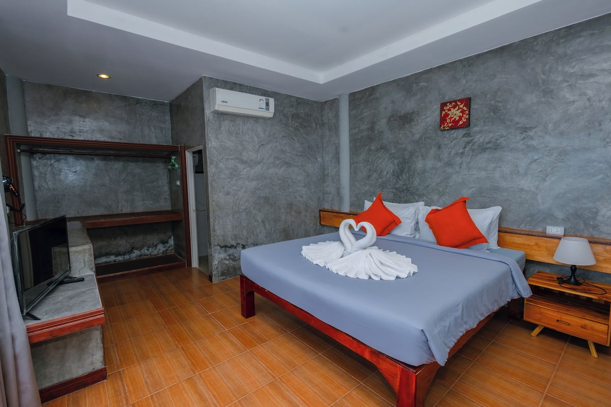 Quarto de hotel com cama, televisão, um banco de madeira e ar condicionado fixado na parede.