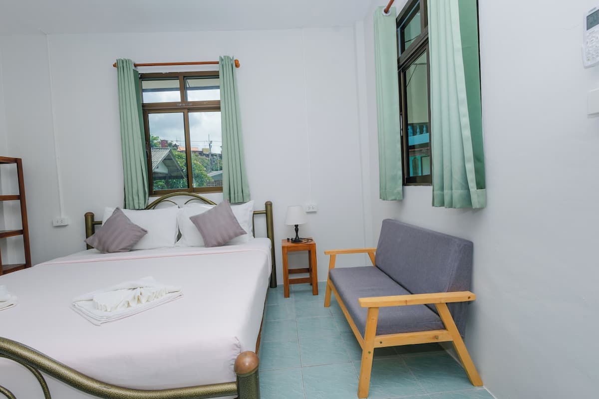 Quarto com cama, cadeira de madeira, mesa de cabeceira e janela com cortinas.