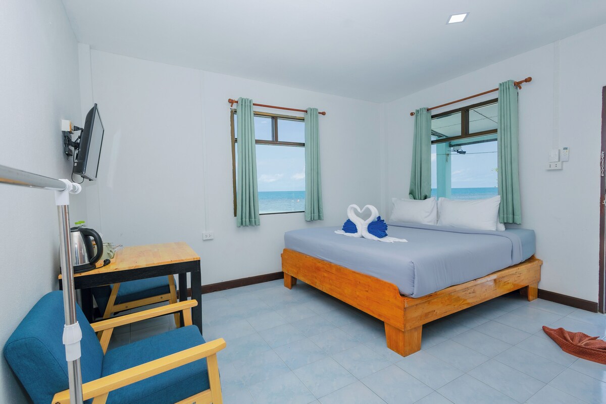 A bedroom with a bed, a desk, a chair, a TV, and windows with curtains.