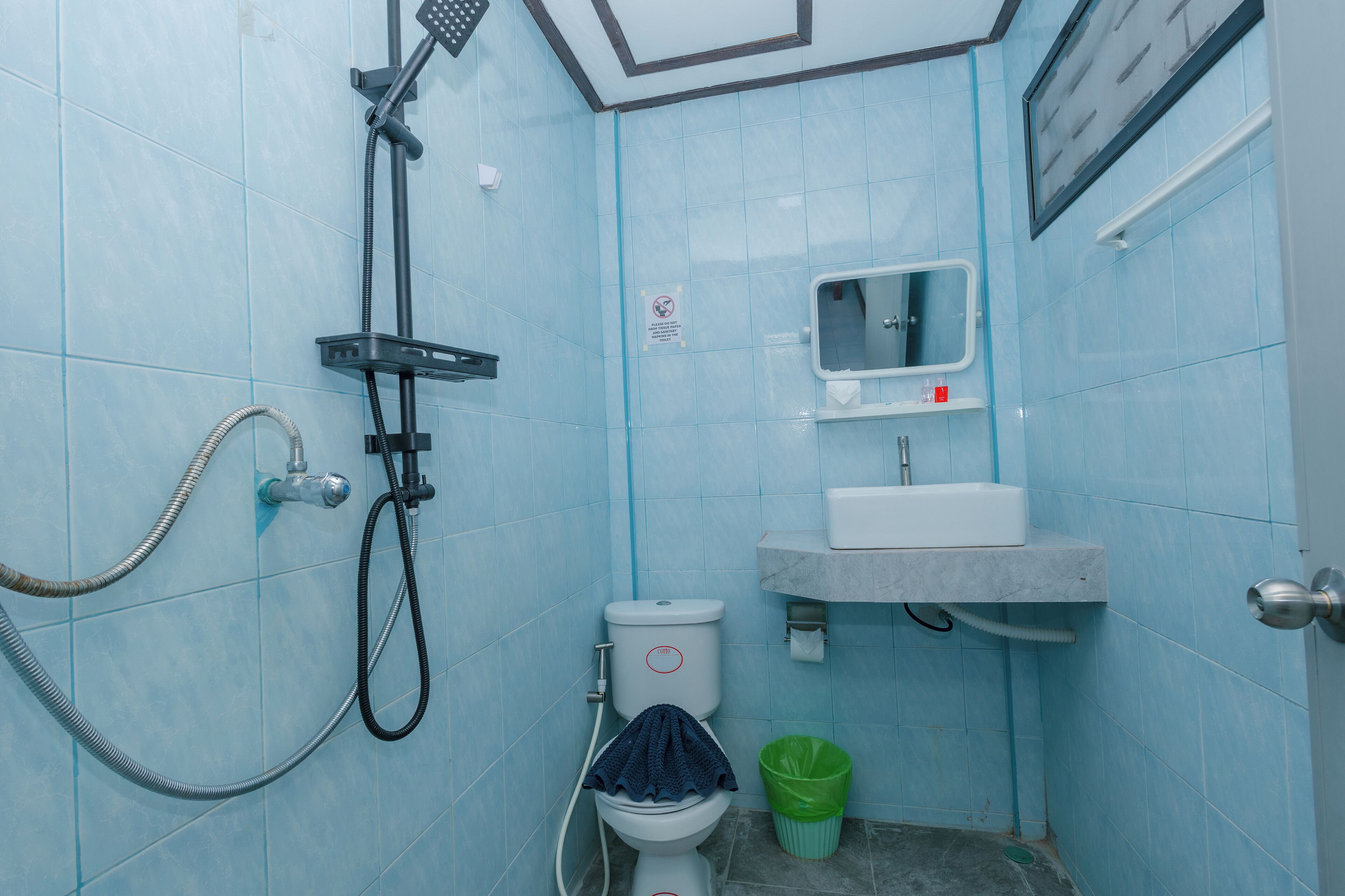 A small bathroom with blue tiles, a toilet, a sink, a mirror, and a shower.