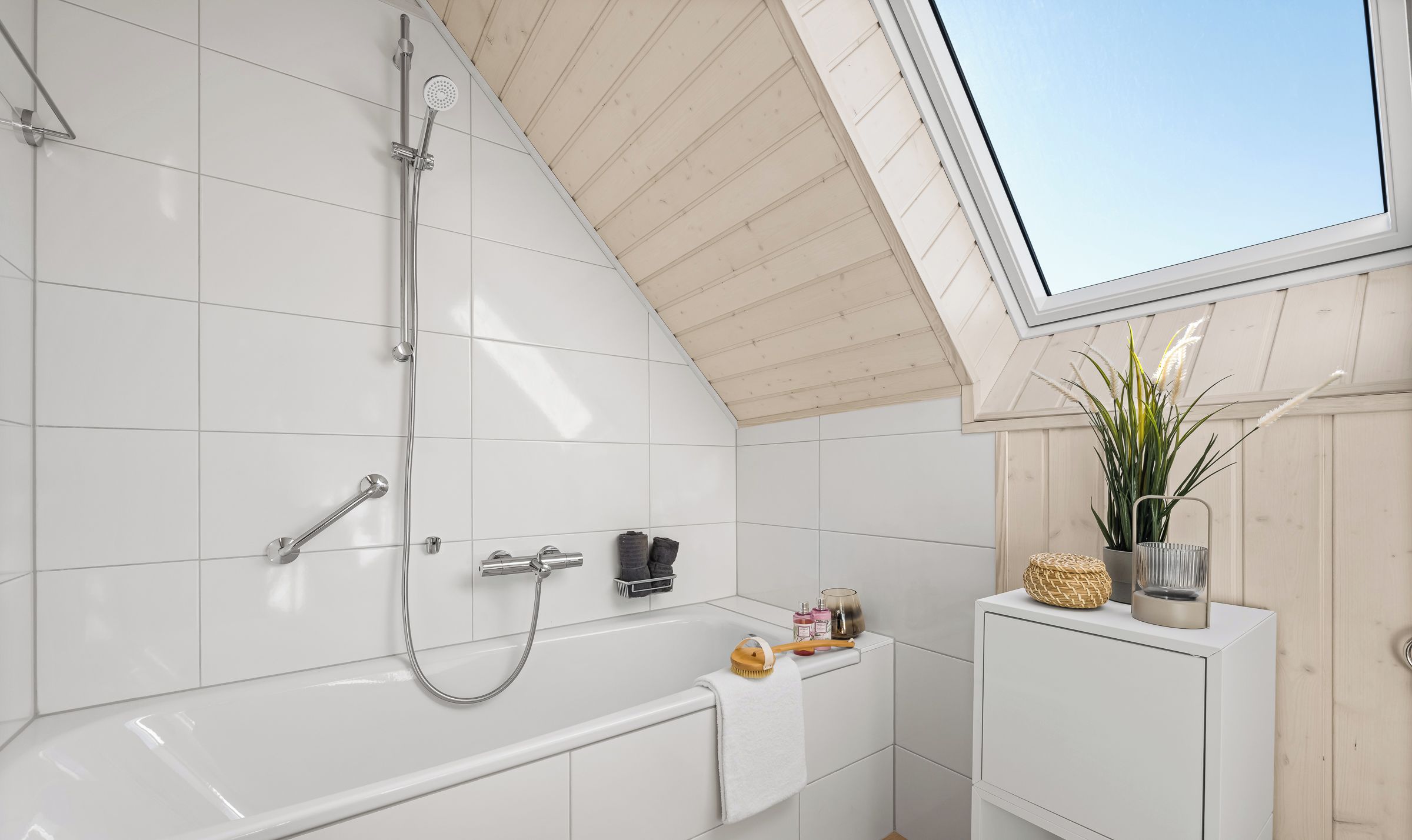 Een moderne badkamer met dakraam, een badkuip, een douche en een klein kastje met toiletartikelen.