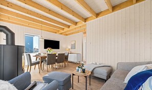A modern living room with a wooden ceiling, a dining area with a table and chairs, and a sofa with a decorative pillow.