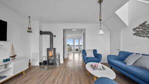 A modern living room with a fireplace, blue sofas, and a wooden floor. - Morgenlicht - Maisonette Apartment, Terrace, Infrared Sauna, Whirlpool, Sea View (Olpenitz)