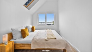 A bedroom with a bed, a nightstand, a lamp, and a window with a view. - Morgenlicht - Maisonette Apartment, Terrace, Infrared Sauna, Whirlpool, Sea View (Olpenitz)