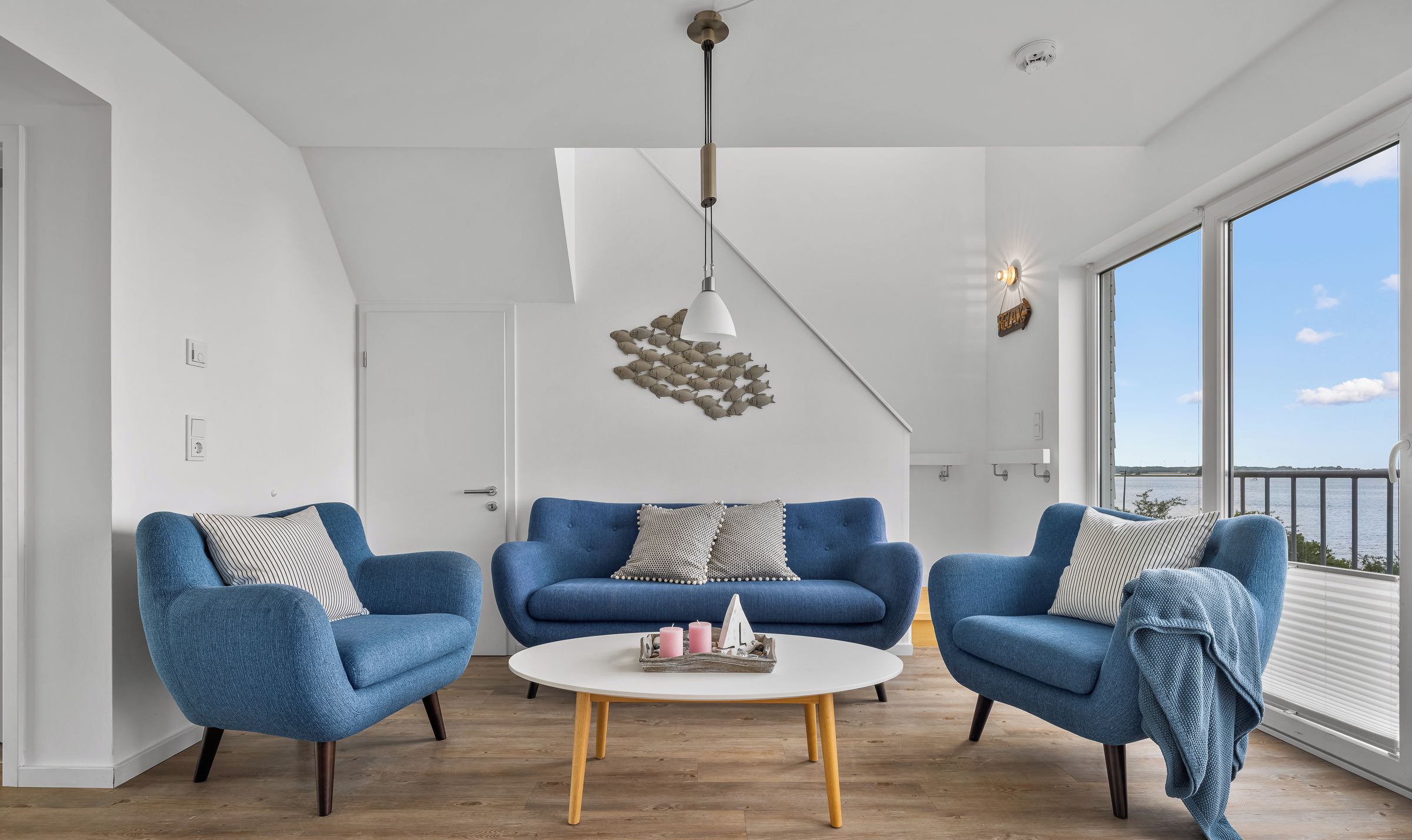 A modern living room with a blue sofa set, a white coffee table, and a hanging light fixture.