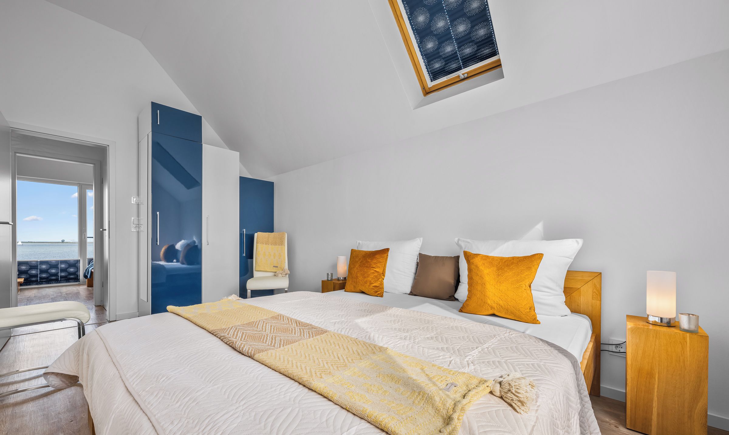 A modern bedroom with a large bed, a view of the sea, and a skylight.