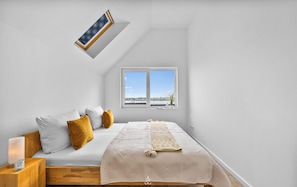 Une chambre à coucher avec un lit, une table de chevet, une lampe et une fenêtre donnant sur un beau paysage.