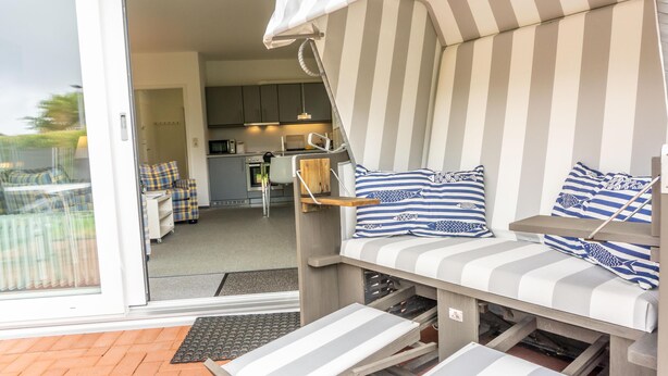 A compact living space with a kitchenette, a striped sofa with cushions, and a sliding door leading to an outdoor area.