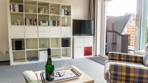 A living room with a bookshelf, a flat-screen TV, a plaid sofa, and a bottle of champagne on a tray.