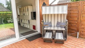 A cozy outdoor seating area with a striped canopy, cushioned chairs, and a television.