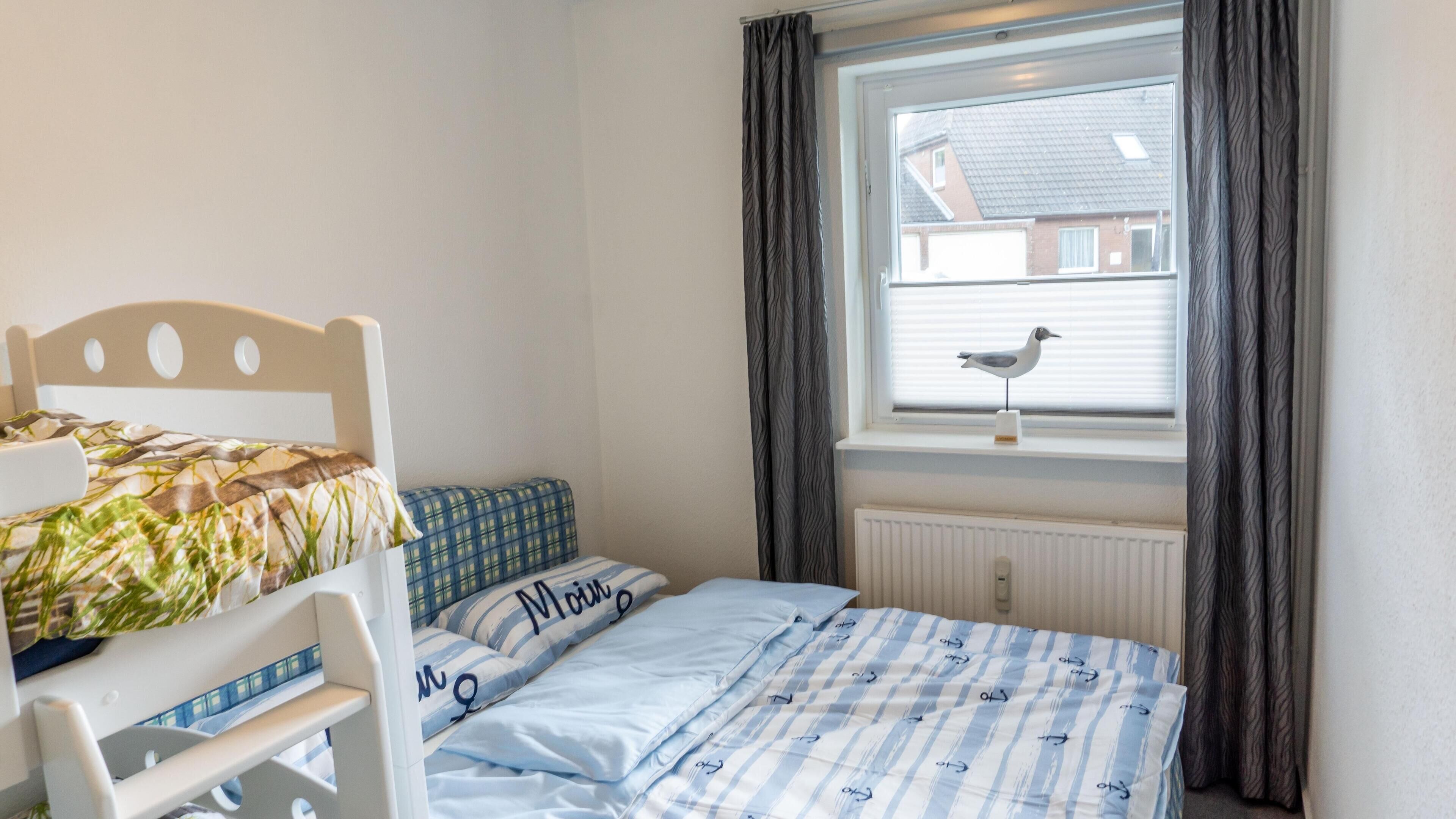 Une chambre avec un lit superposé, un lit simple, une fenêtre avec des rideaux et un radiateur.