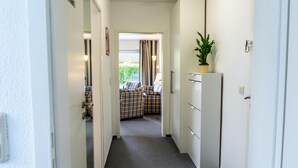 A narrow hallway with a door on the left, a wardrobe on the right, and a room with plaid furniture in the background.