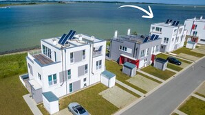 A modern residential building with solar panels, a parking area, and a view of a lake.