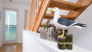 A seagull perched on a wooden structure with a view of a balcony and indoor space.
