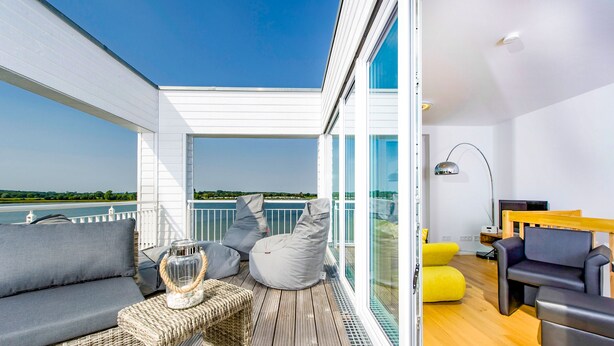 A balcony with a sofa, cushions, and a glass table.