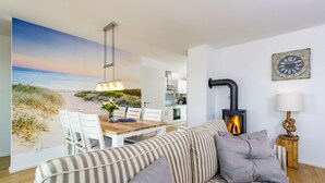 A cozy living room with a sofa, a dining table with chairs, a fireplace, and a wall-mounted clock.