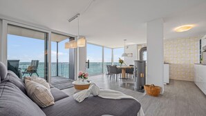 Uma sala de estar moderna e espaçosa, com um sofá grande, uma mesa de jantar e vista para o mar.