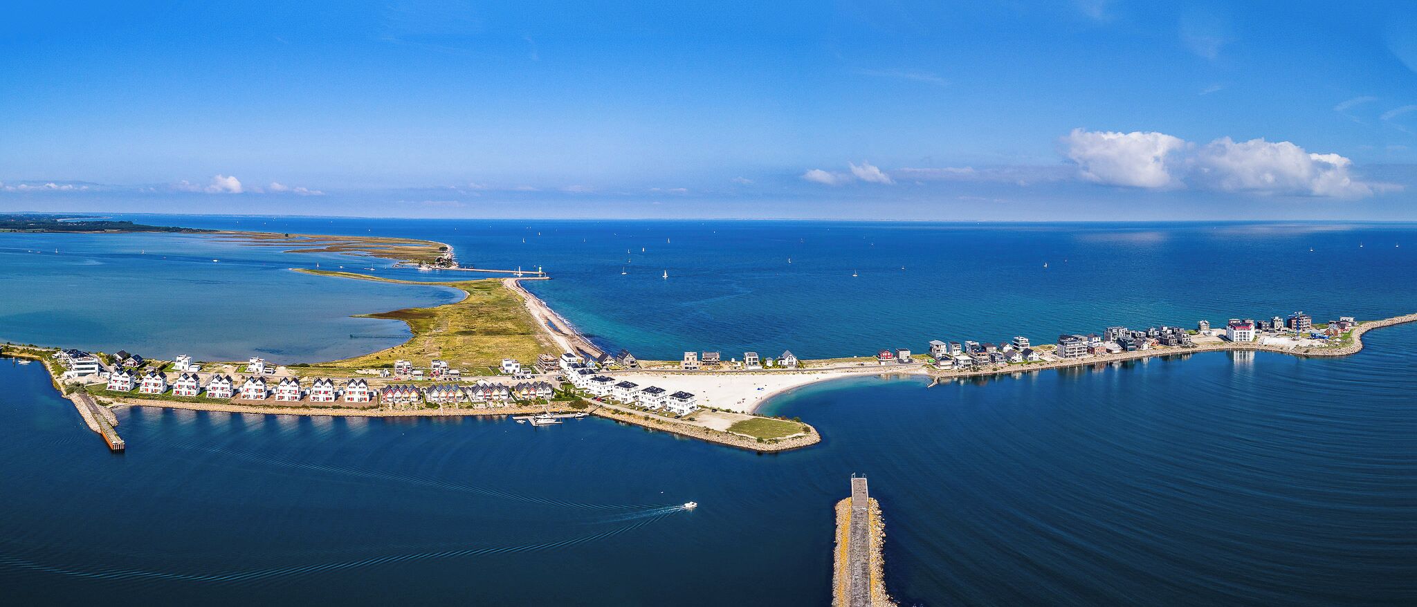 An aerial view of a coastal resort with a marina, beachfront properties, and a lighthouse.