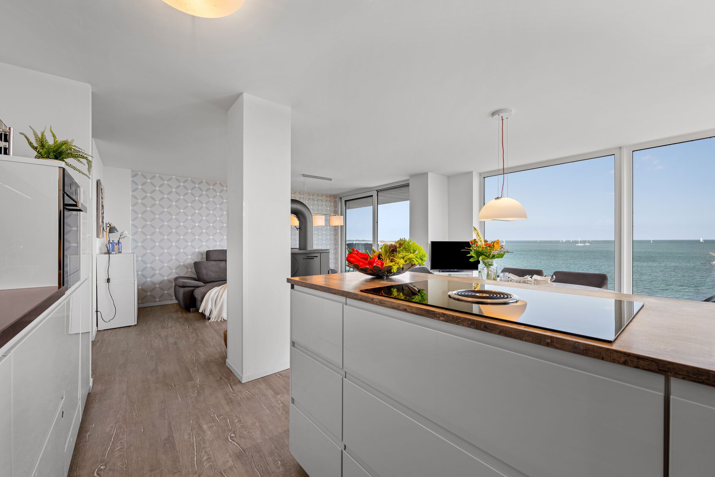 A modern kitchen with a large island, a dining area with a view of the sea, and a cozy seating area with a fireplace.
