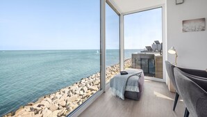 Quarto moderno com uma grande janela com vista para um litoral rochoso e o mar.