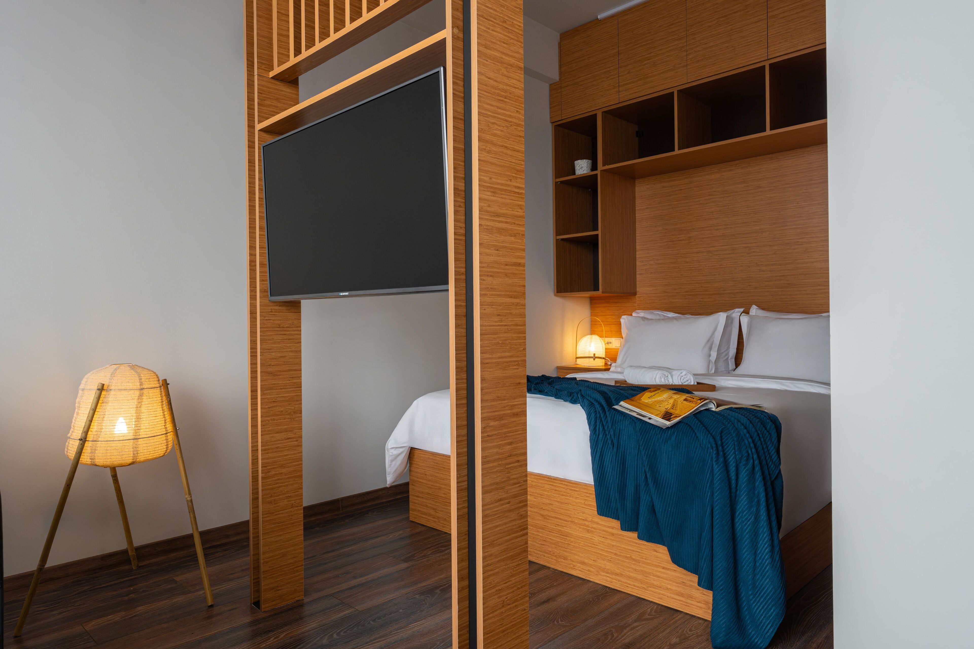 A hotel room with a bed, bedside table, lamp, and a large screen.