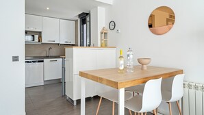 A modern kitchen with white cabinets, a wooden countertop, and a dining area with a wooden table and white chairs. - Appartamento di fronte al mare, piscina, aria condizionata, parcheggio ascensore (El Mas Mel)