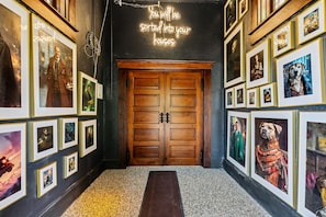 Un couloir aux murs ornés de tableaux encadrés, une porte en bois et un panneau lumineux au-dessus.